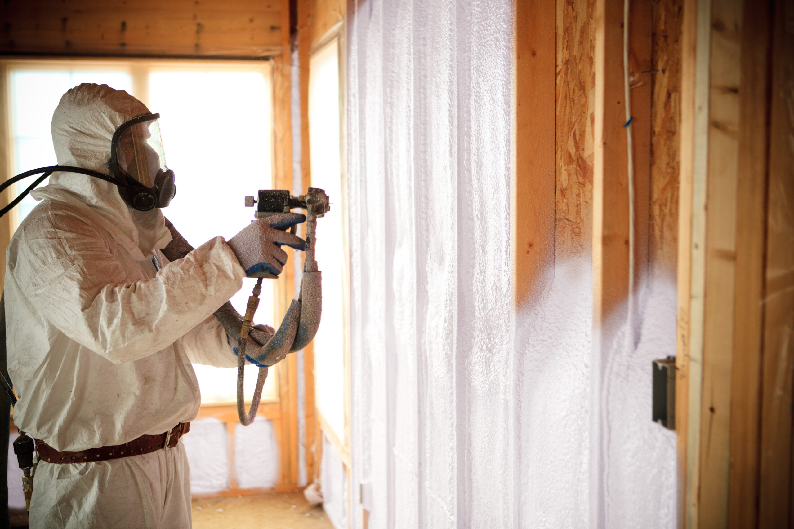 Installer spraying open-cell foam insulation into wall cavities